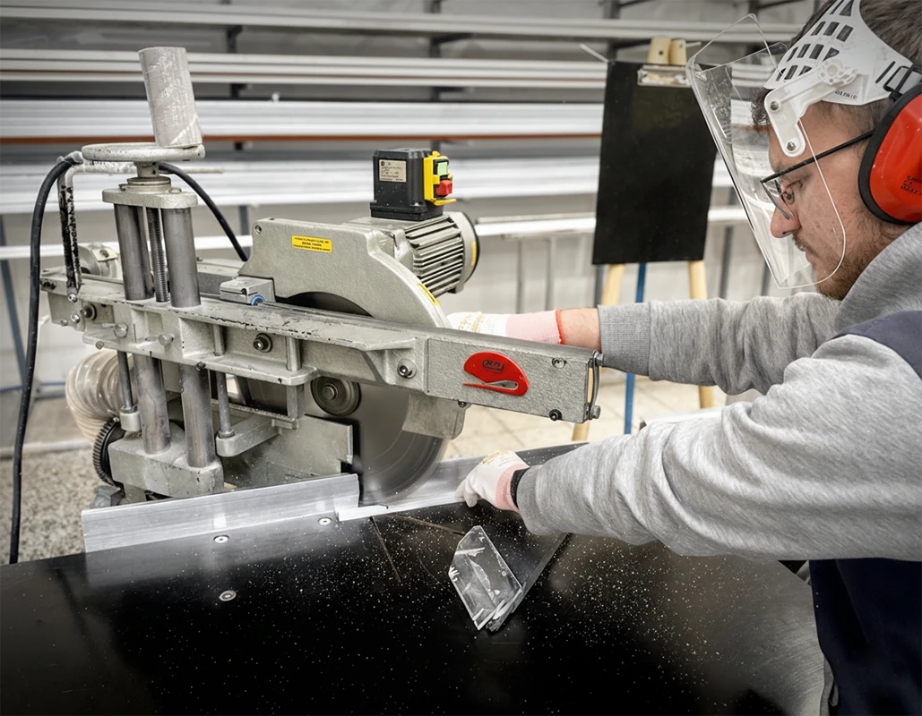 Pracovník řeže materiál na výrobu sítí proti hmyzu vedle přehledu typů síťoviny – šedá, černá a odolná PET